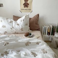 a bed with white sheets and teddy bears on it, next to a bookshelf