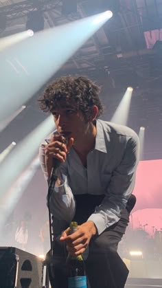 a man holding a microphone while standing next to a stage with lights on the ceiling