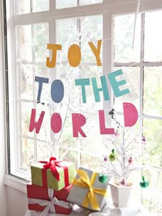 christmas presents are piled up in front of a window with the words joy to the world on it