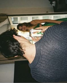 a man taking a photo of himself in the fridge with his cell phone while two other people look on