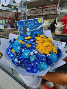 a bouquet of blue and yellow flowers in front of a store window with a painting on it