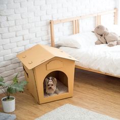 a dog in a cardboard house on the floor next to a bed and potted plant