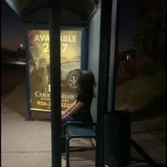 a woman sitting on a chair in front of a bus stop sign at night time