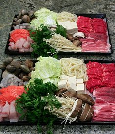 two trays filled with meat and vegetables on top of a stone floor next to each other