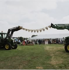 two green tractors parked next to each other on top of a lush green field under a white tent