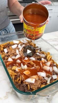 a person pouring sauce onto a casserole dish with onions and meat in it