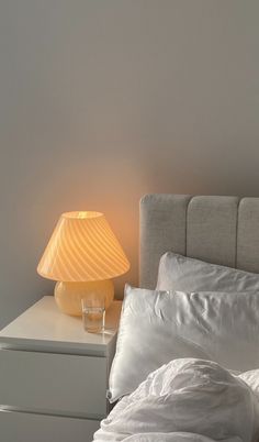 a bed with white sheets and pillows next to a lamp on a nightstand in a bedroom