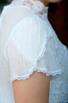 a close up of a woman wearing a white shirt with lace on the shoulders and sleeves