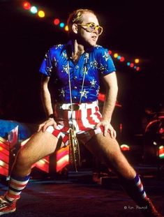 a man in patriotic shorts and sunglasses sitting on stage with an american flag shirt over his body