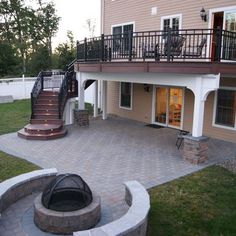 a patio with a fire pit in the middle and stairs leading up to an upper level deck