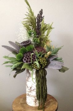 a white vase filled with lots of different types of flowers and greenery sitting on top of a wooden table