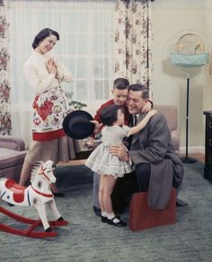 black and white photograph of family in living room with rocking horse, man holding child