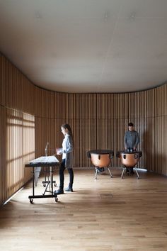 two people standing in an empty room with wooden slats on the wall behind them