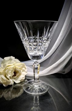 an empty wine glass sitting next to a flower on a black tablecloth with white fabric behind it