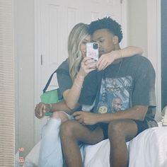 a man and woman sitting on top of a bed taking a selfie with their cell phone