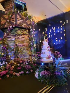 a wedding cake sitting on top of a table in front of a wall with flowers