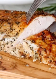 a piece of chicken being cut with a knife and fork on a wooden cutting board