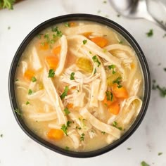 a bowl filled with chicken noodle soup on top of a white counter next to a spoon