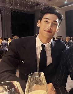 a man in a suit and tie sitting at a table with a glass of wine