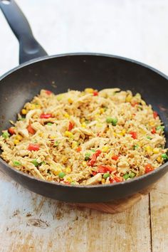 a skillet filled with rice and vegetables on top of a wooden table next to a fork