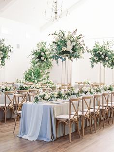 the tables are set up with white flowers and greenery on them for an elegant wedding reception