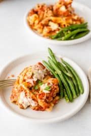 two white plates topped with green beans and lasagna casserole next to a fork