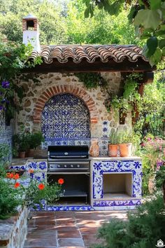 an outdoor kitchen with blue and white tiles on the outside wall, surrounded by flowers