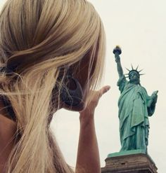 a woman with headphones on looking at the statue of liberty in new york city