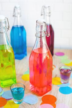 three bottles filled with liquid sitting on top of a table next to glasses and confetti