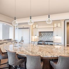 a large kitchen with marble counter tops and white cabinets, along with bar stools