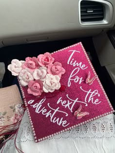 a pink sign that says time for the adventure with flowers on it sitting in front of a car