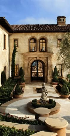 a large house with a fountain in front of it and lots of plants around the entrance