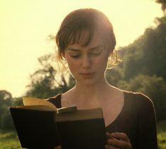 a woman is reading a book outside in the grass and looking down at her face