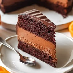 a slice of chocolate cake on a white plate with a fork and oranges in the background