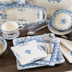 blue and white dinnerware set on wooden table with utensils, napkins and silverware