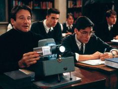 two men sitting at a table with an old camera in front of them and another man writing