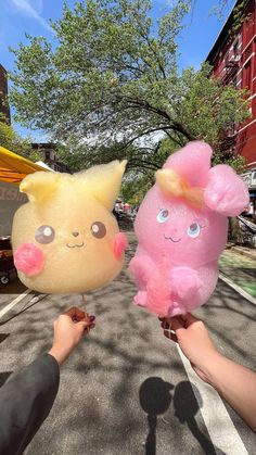 two stuffed animals are being held in the air by someone's hand on a city street