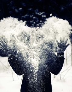 a person standing in the snow holding their hands up to their face and throwing snow into the air