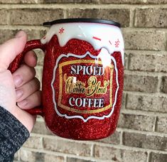 a person holding a red and white coffee mug in front of a brick wall with writing on it