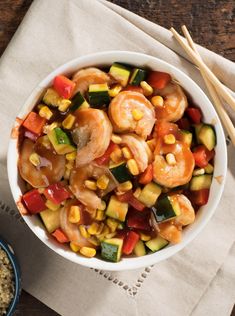 a bowl filled with shrimp and veggies next to chopsticks on top of a table