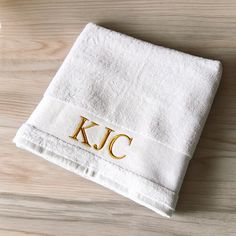 a white towel with the letter k c on it sitting on top of a wooden table