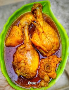 a person holding a green bowl filled with chicken wings and sauce on top of it