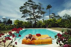 a woman laying on an inflatable mattress next to a pool with red flowers