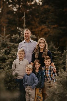 a family posing for a photo in front of christmas trees at the tree farm with their two children