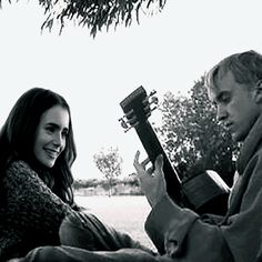 a man and woman are sitting under a tree playing the ukulele guitar together