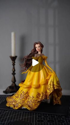 a doll in a yellow dress sitting on a table next to a candelabra