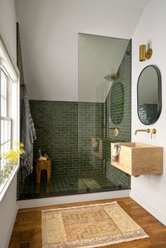 a bathroom with green tile and wooden flooring, along with a rug on the floor