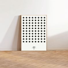 a white poster with black dots on it in front of a wooden floor and wall