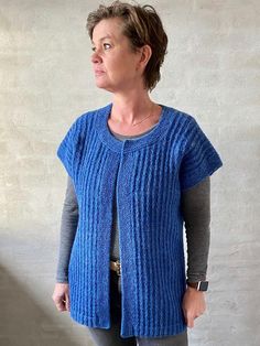 a woman standing in front of a wall wearing a blue sweater