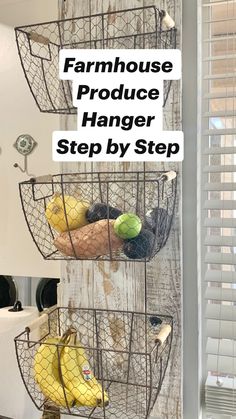 three wire baskets holding fruit and vegetables are hanging on the wall next to a window